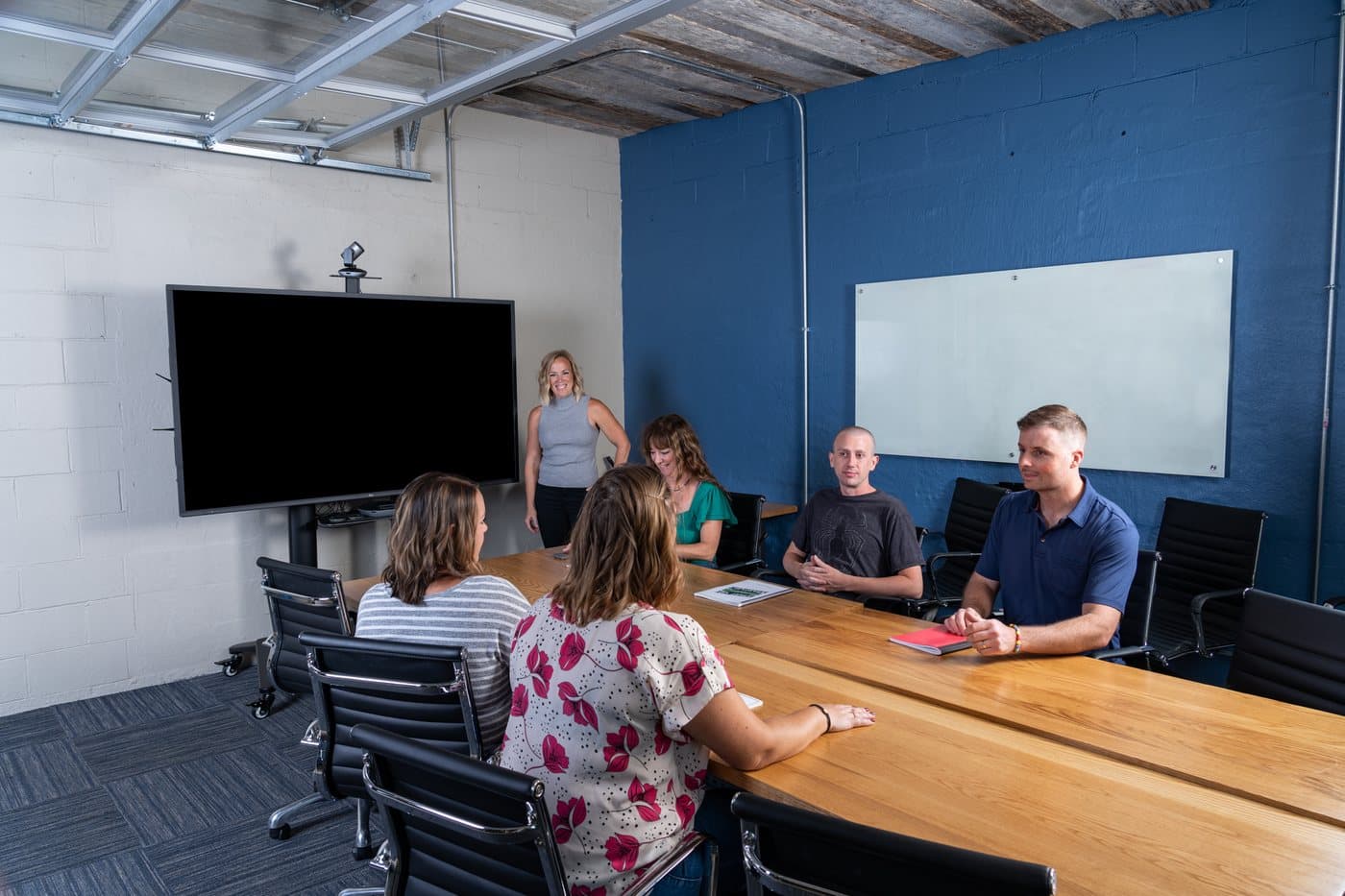 A group meeting around the long boardroom table under a screen