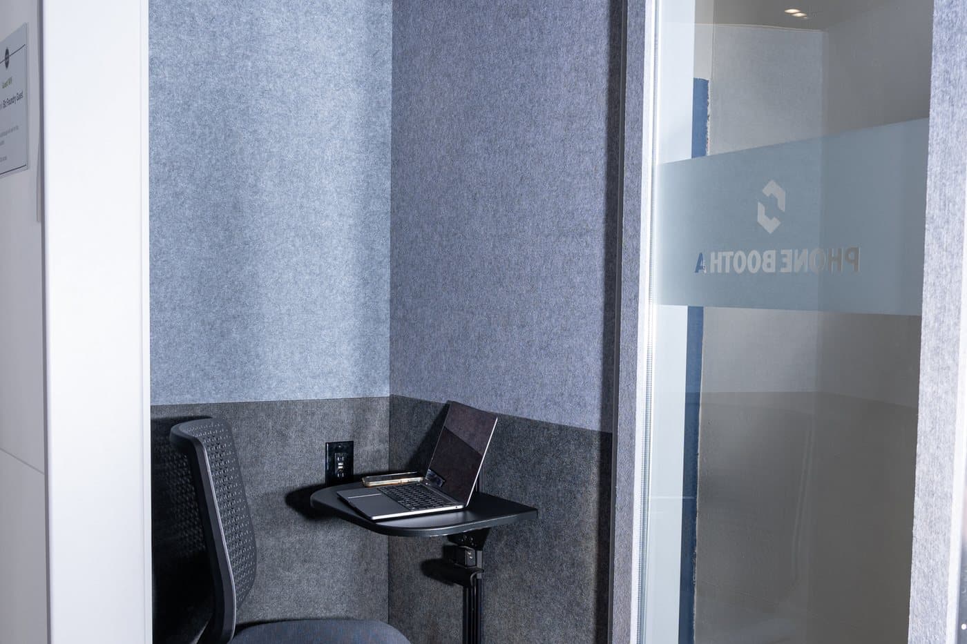 Inside a soundproofed phone booth with a small desk and stool