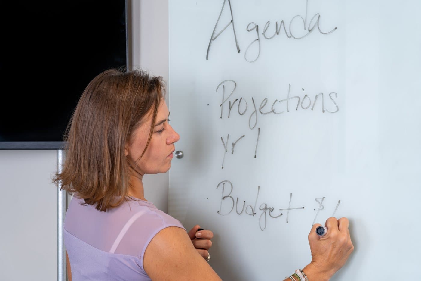 A member writing an agenda on a glass whiteboard