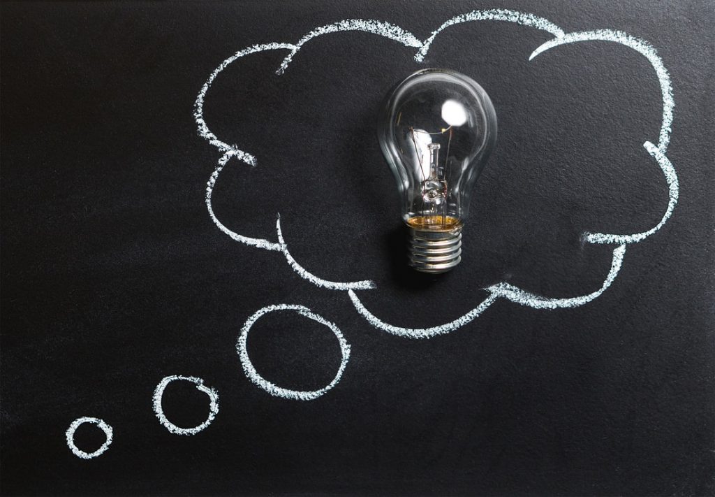 An image of a blackboard with a chalk drawn thought bubble Inside the thought bubble sits a real glass lightbulb