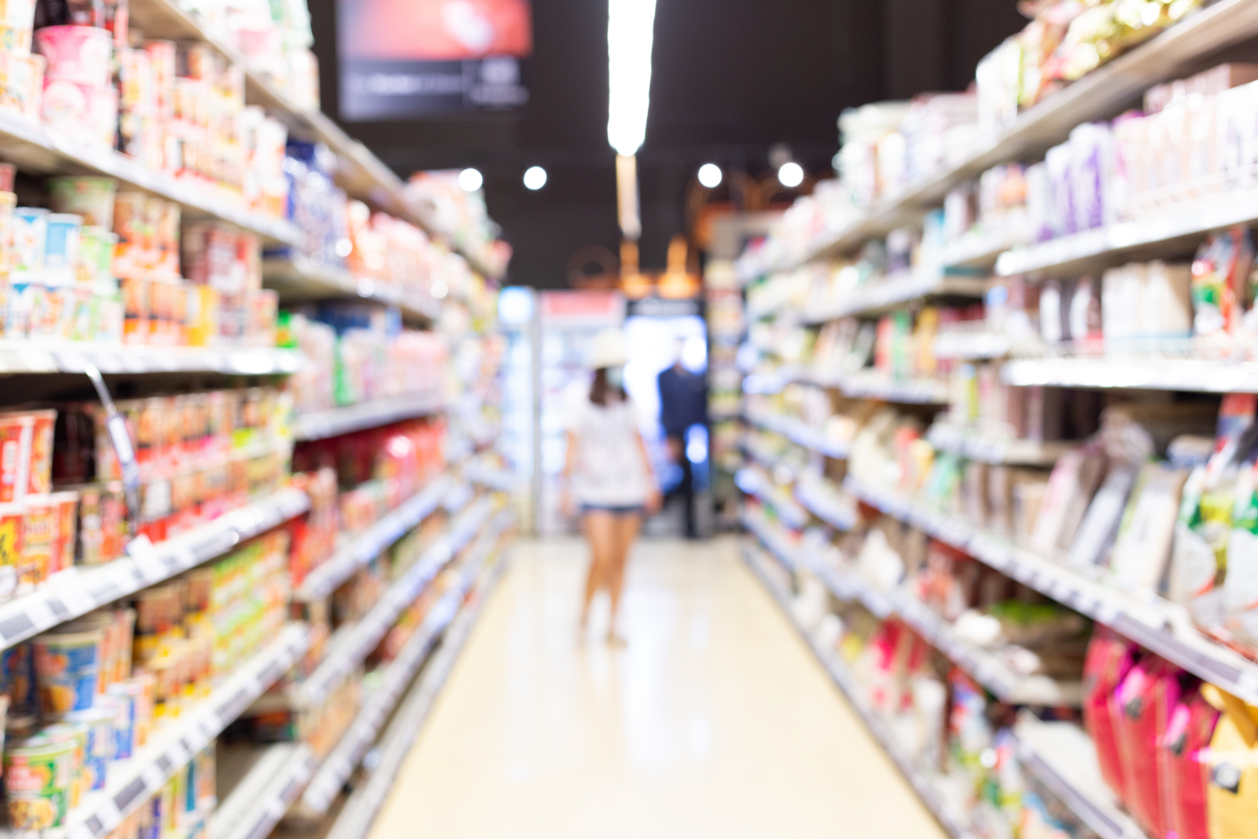 Photo of customers walking down the aisle of a grocery store surrounded by consumer packaged goods